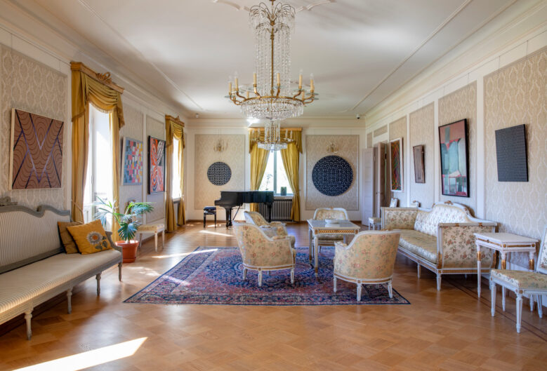 Elegant sal i Söderlångviks museum med kristallkronor, historiska möbler, konstverk på väggarna och en flygel i fonden.